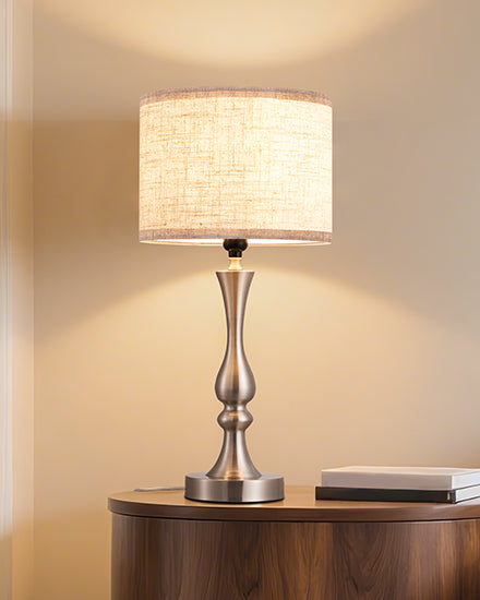 Table lamp with a textured shade on a wooden surface, emitting a warm glow.