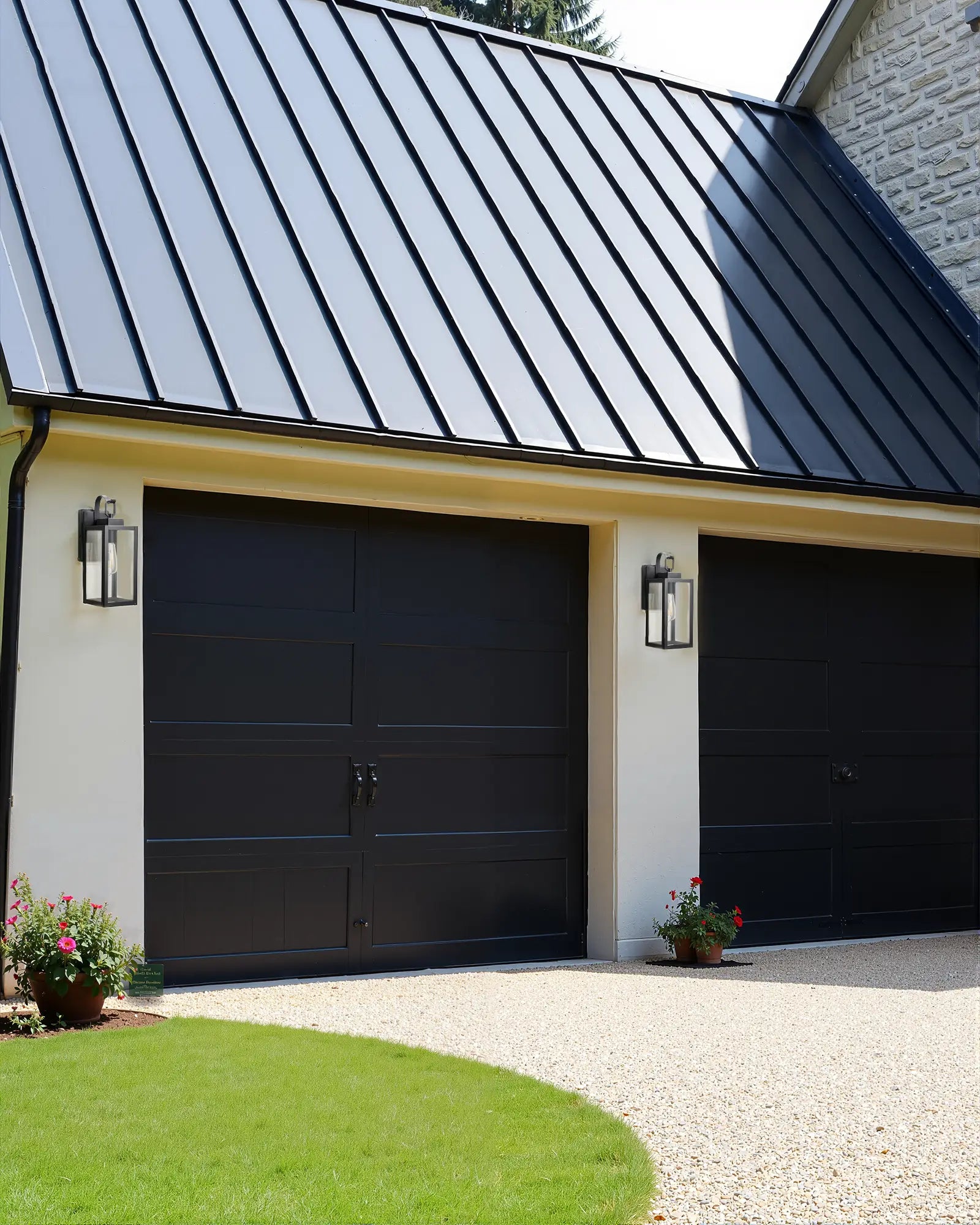 Black garage doors on a house with a metal roof, Dusk to Dawn Outdoor Wall Lantern,and green grass.