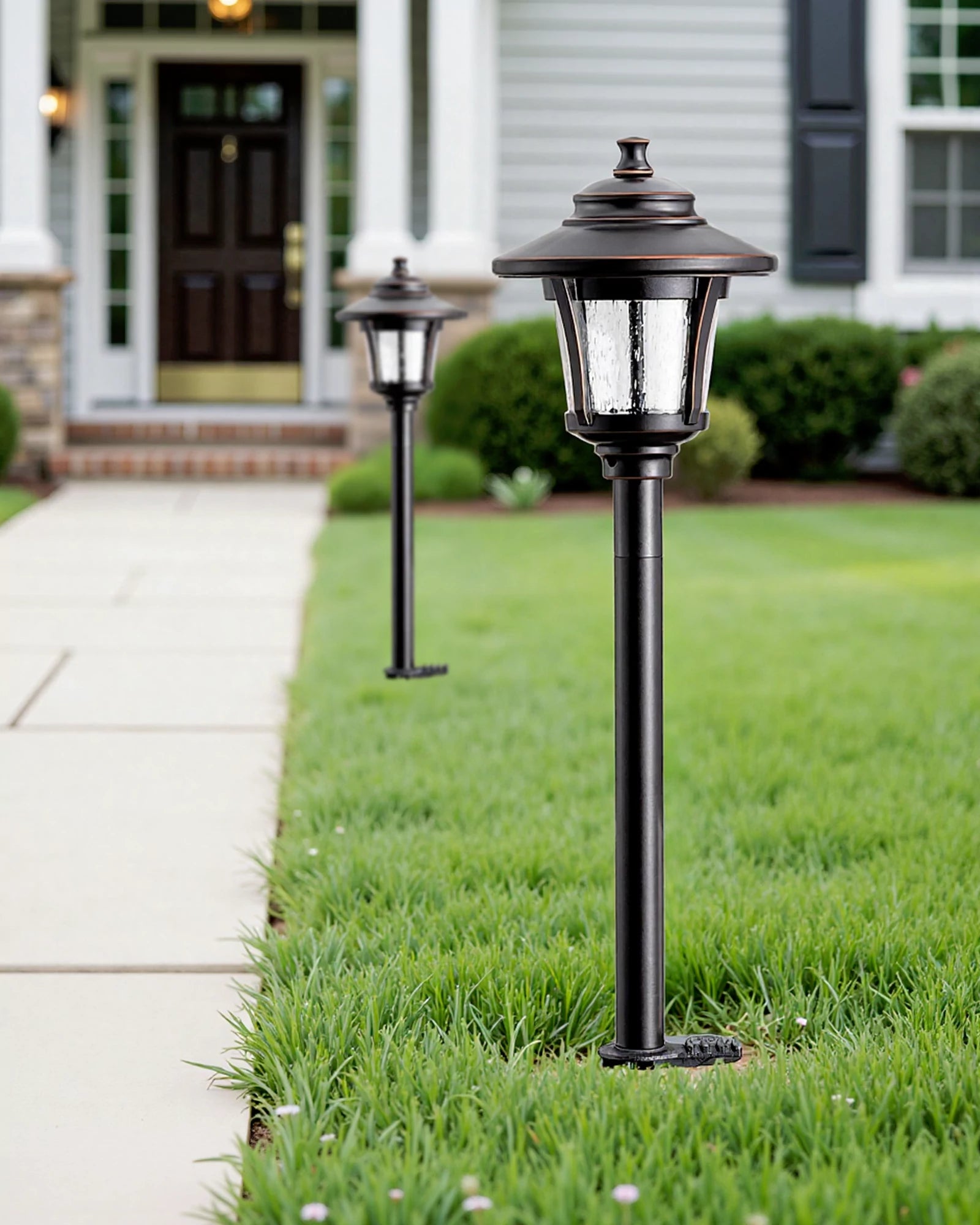 Two black outdoor lamps on grass with a house in the background