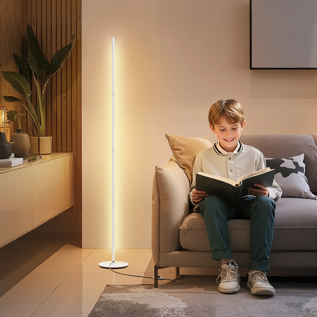 Child reading a book in a cozy living room with a floor lamp.