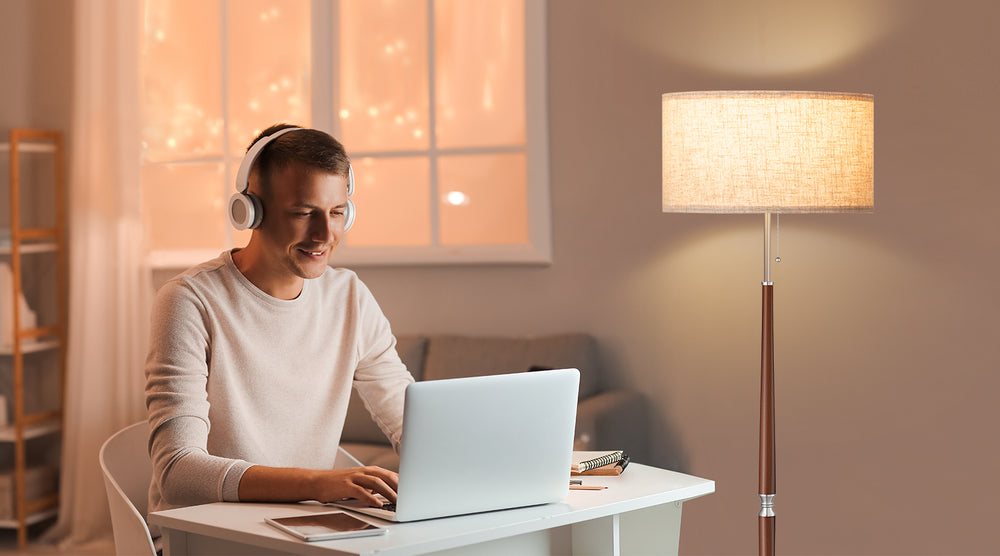 Person working on a laptop in a cozy room with a lamp and window in the background