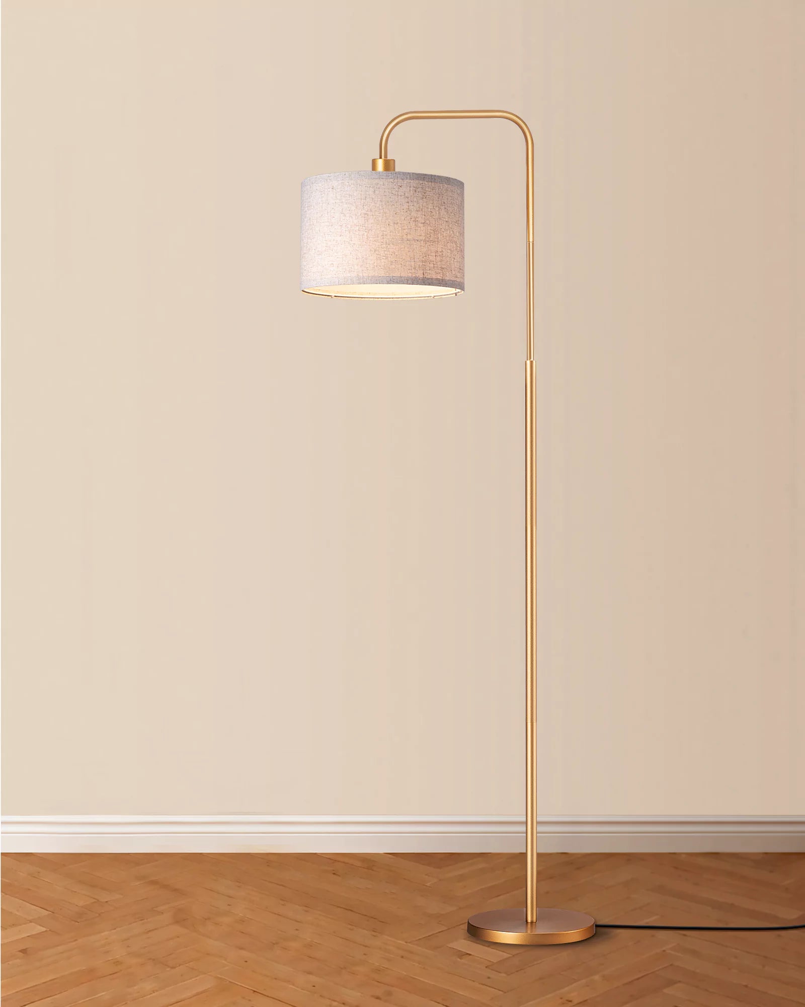 Floor lamp with gold base and beige shade on a wooden floor against a beige wall