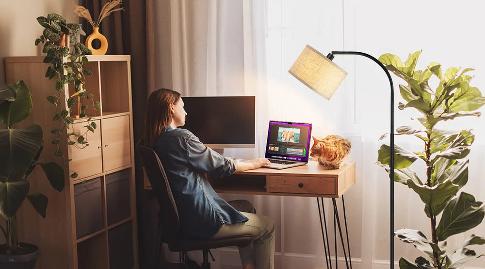 Person working at a desk with a computer and laptop, surrounded by plants and a Arched Hanging Floor Lamp in a home office setting.