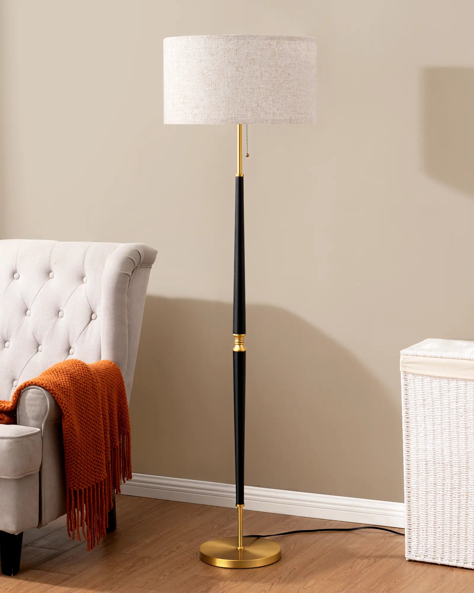 Floor lamp with a white shade and black and gold base in a room with a chair and ottoman.