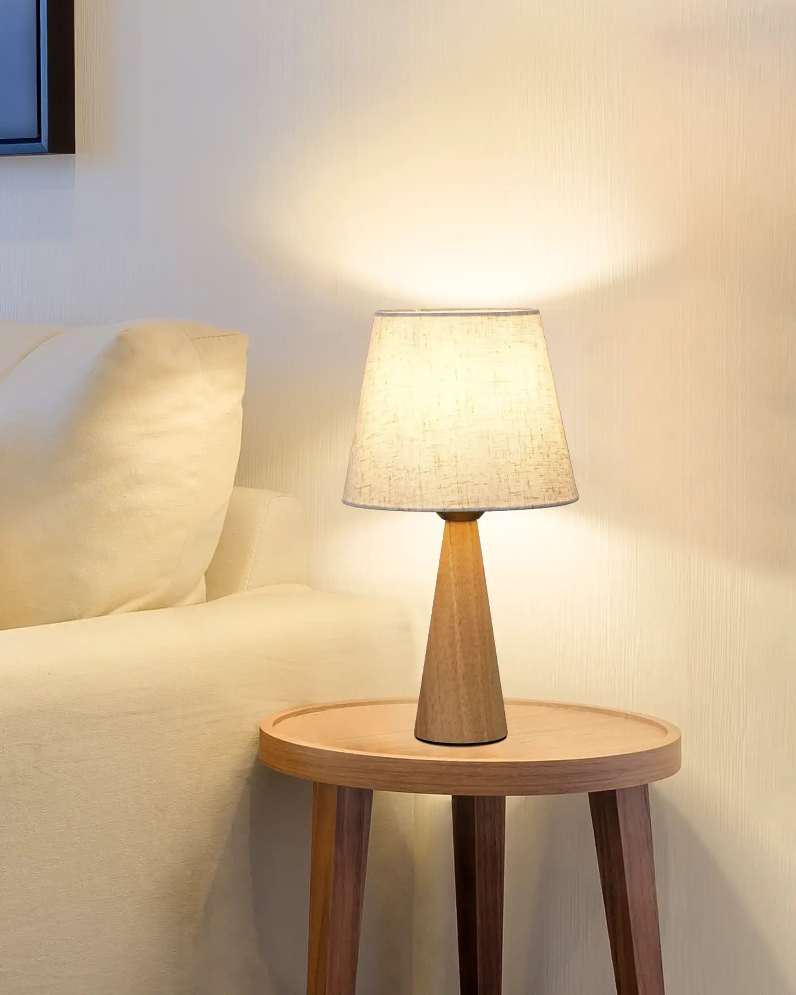 Wooden side table with a Linen Table Lamp next to a sofa in a room.
