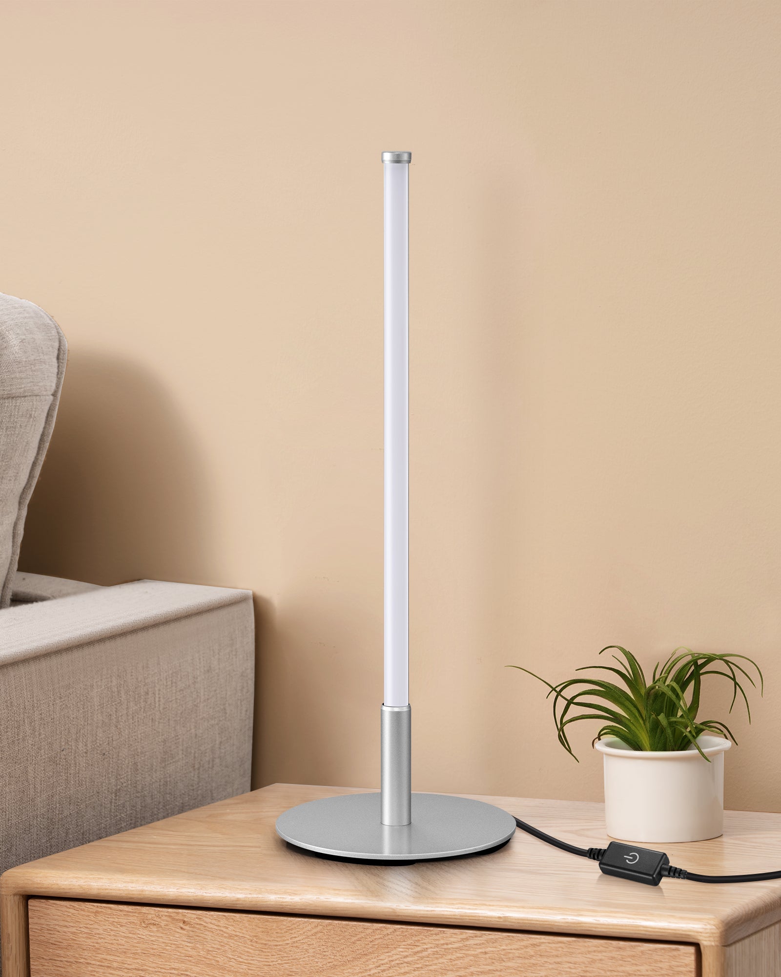 Modern LED table lamp on a wooden surface with a beige wall and plant in the background