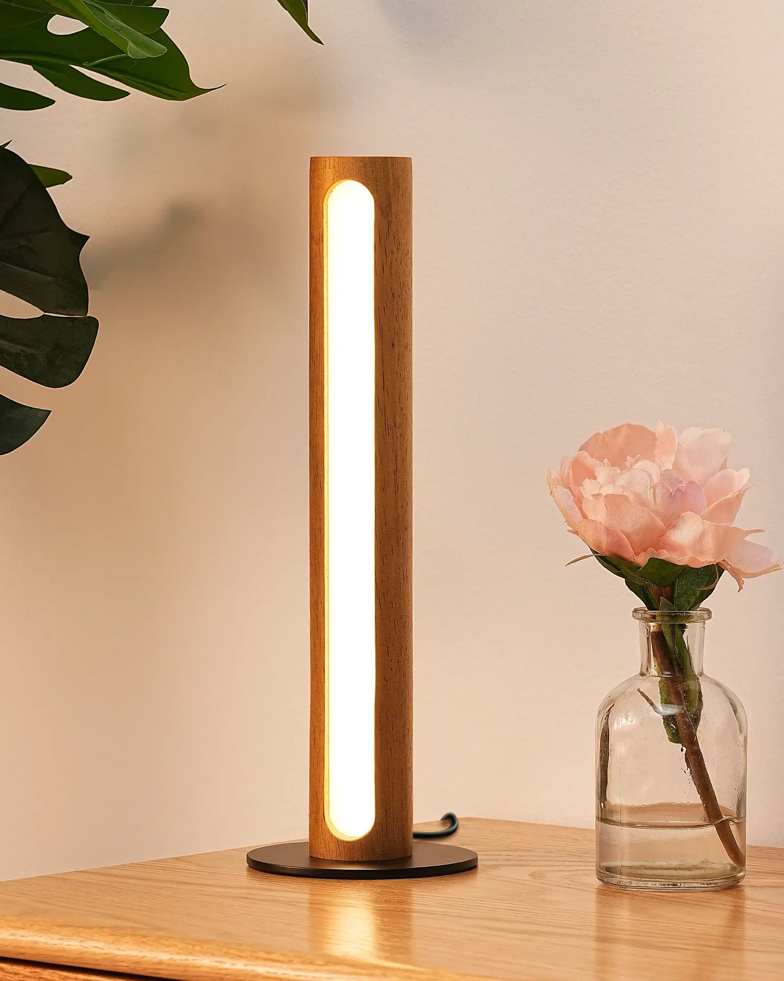 Wooden table lamp on a wooden surface with a vase of flowers and leaves in the background
