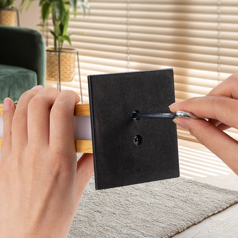 Person holding a black square object with a wooden handle in a home setting.