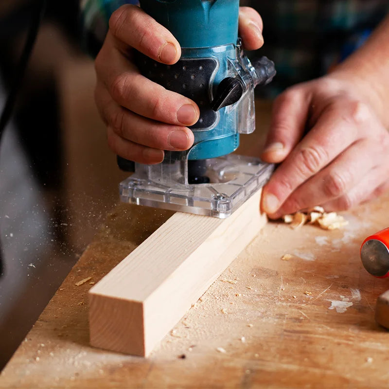 Person using a power tool on a piece of wood with a wooden surface in the background