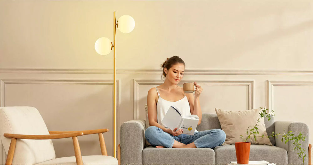 Woman reading a book and drinking coffee in a cozy living room under a Modern Sphere Standing Light.