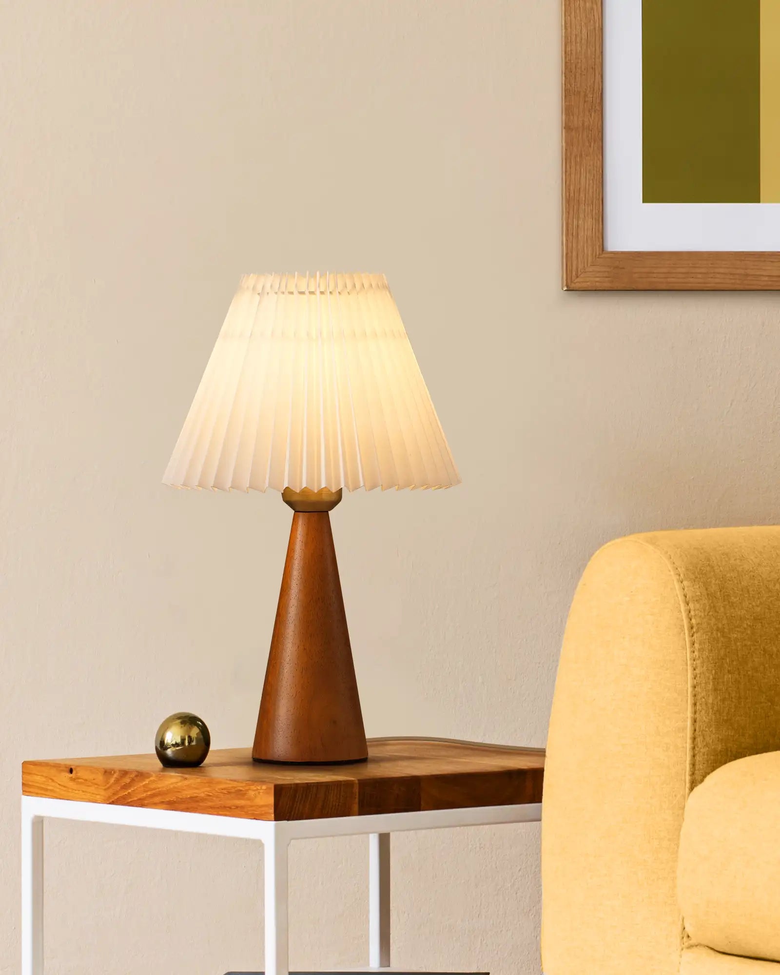 Table lamp with pleated shade on a wooden side table next to a yellow armchair.
