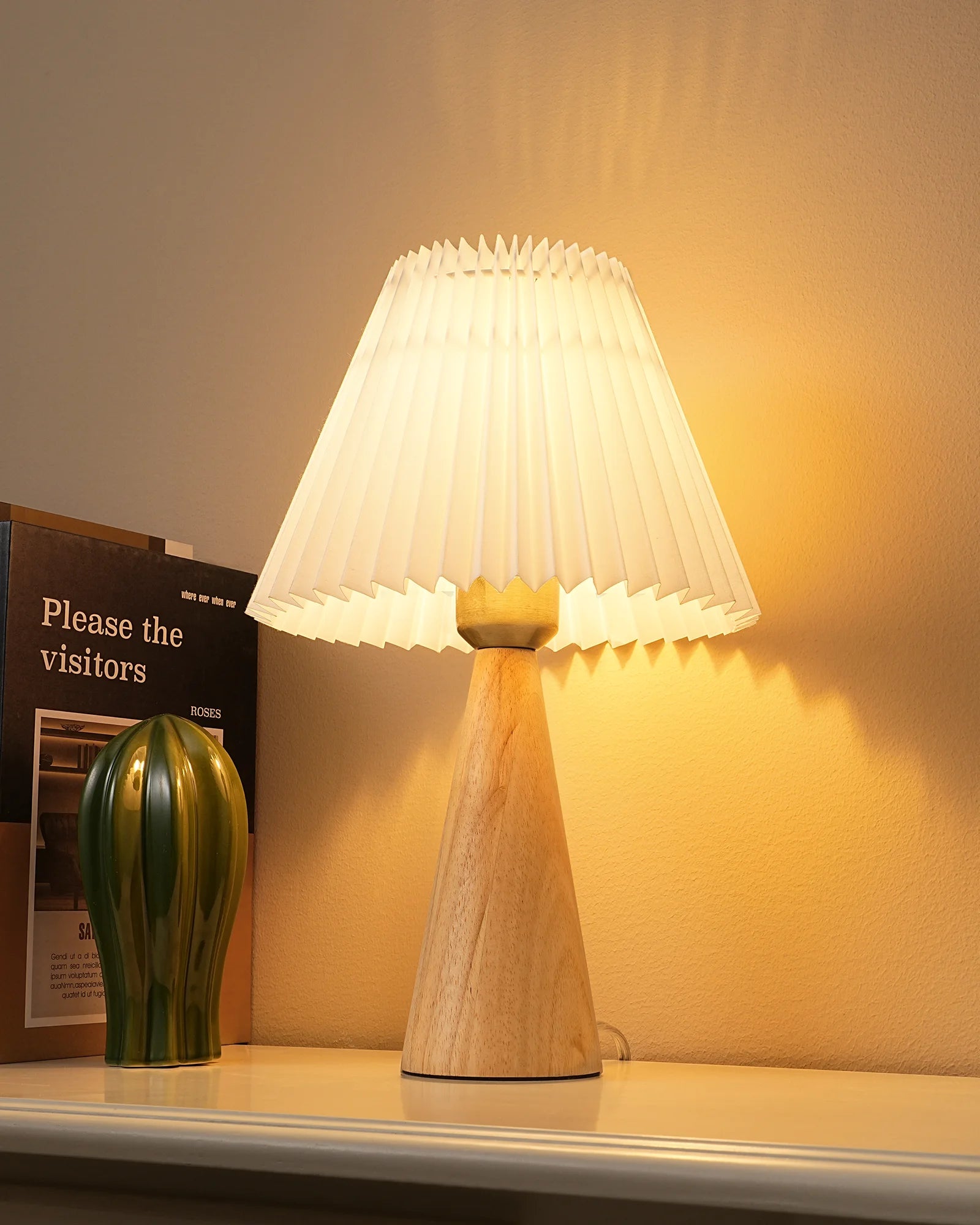 Pleated White Table Lamp with pleated shade on a surface next to a book and small vase.