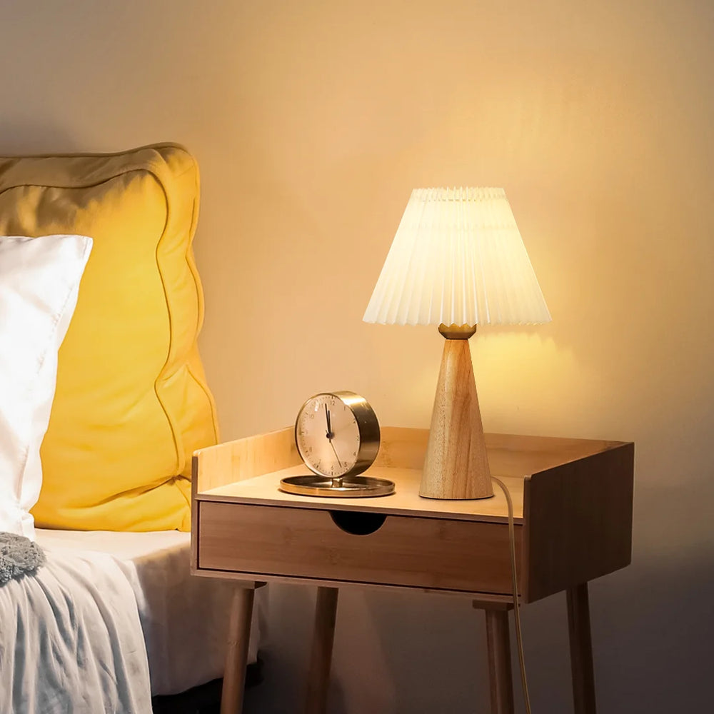 Wooden nightstand with Pleated White Table Lamp and clock next to a bed with yellow pillow