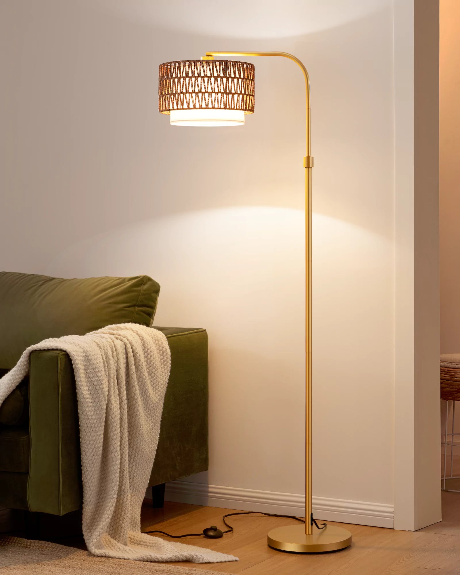 Gold  Rattan Arc Floor Lamp casting light on a green sofa with a blanket in a cozy room.