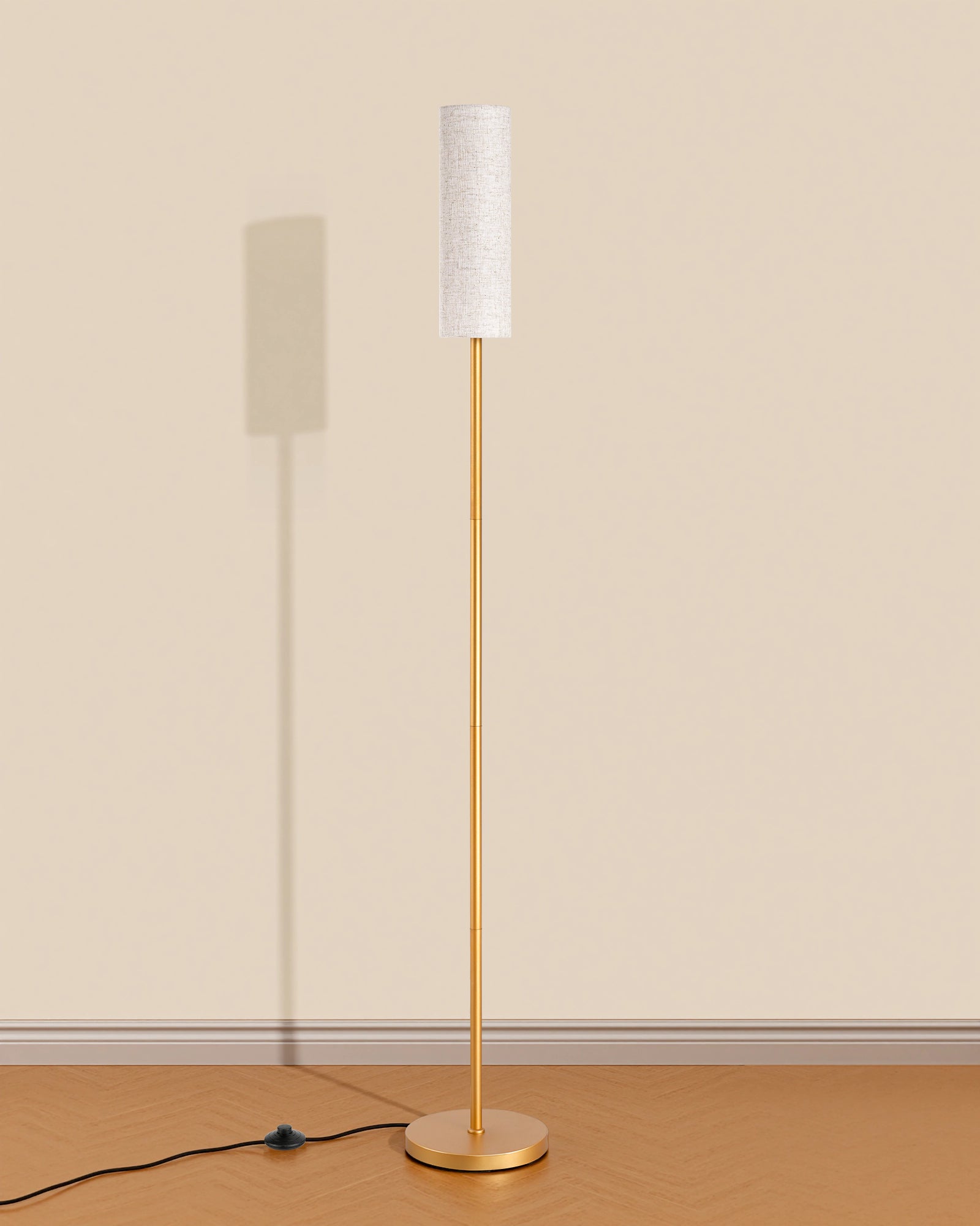 Floor lamp with gold base and white shade on a wooden floor against a beige wall
