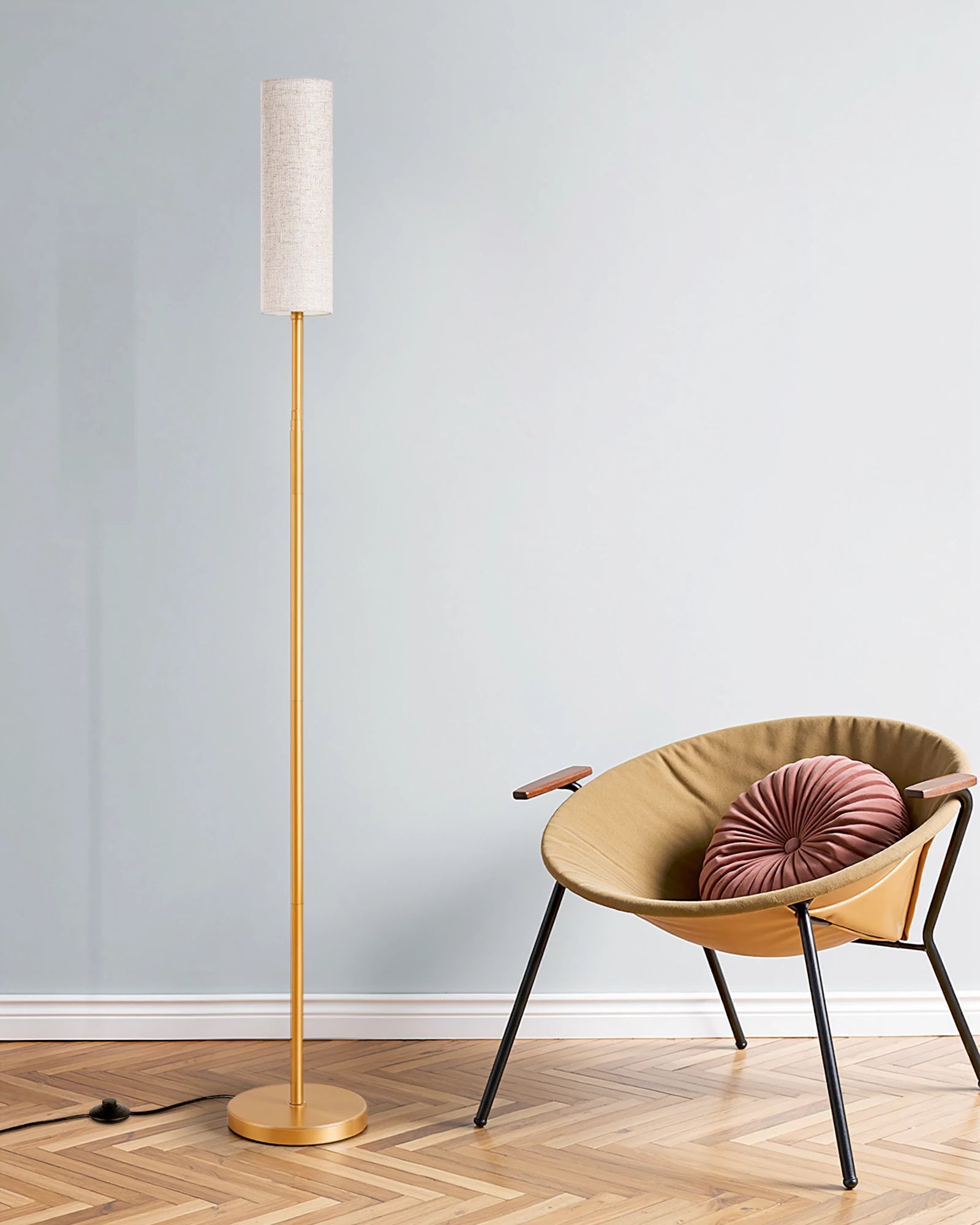 Gold floor lamp next to a chair with a cushion on a wooden floor against a light blue wall.
