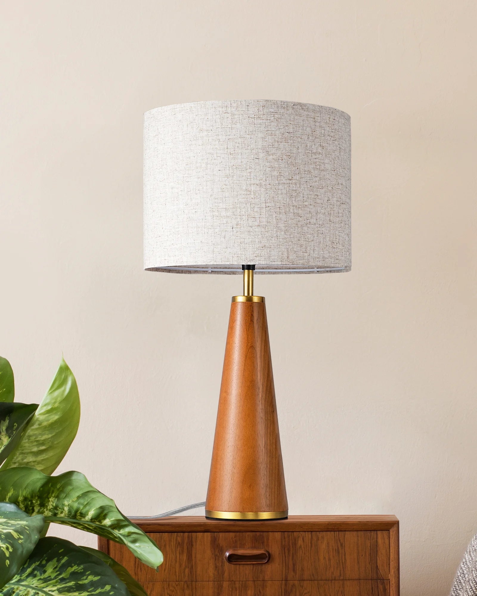 Solid Wood Table Lamp with wooden base and gray shade on a wooden surface with a plant in the foreground.