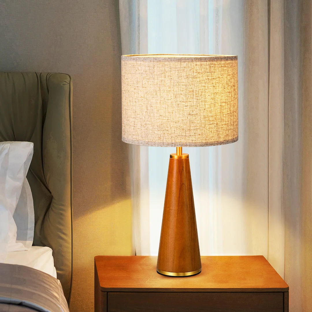 Solid Wood Table Lamp with a beige shade on a nightstand next to a bed.