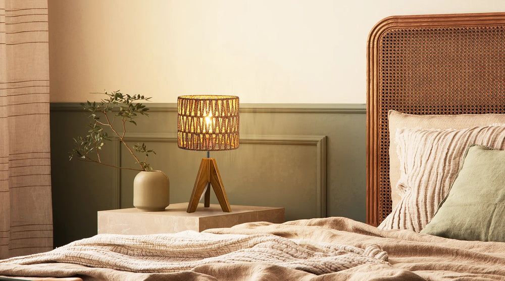 Bedroom scene with a Woven Shade Table Lamp on a nightstand next to a bed with pillows and blankets.